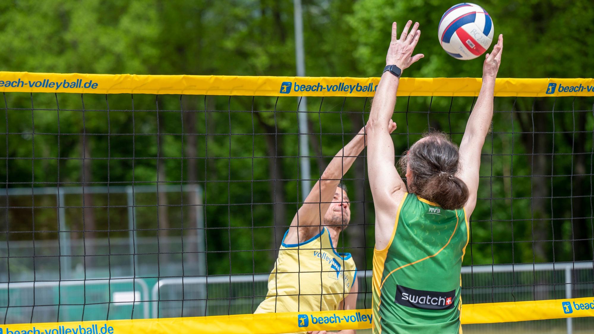 Zwei Beachvolleyballer spielen einen Ball über das Netz.