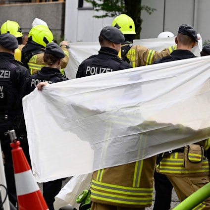 Am Tag der Explosion sind viele Einsatzkräfte der Polizei und der Feuerwehr am Tatort zu sehen. Eine Plane schirmt Blicke von außen teilweise ab.