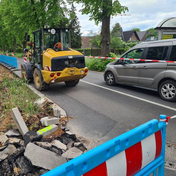 Die Bushaltestelle an der Dansweilerstraße in Glessen wird dargestellt. Ein Baufahrzeug und ein Auto sind vordergründig an einer abgesperrten Baustelle zu sehen.