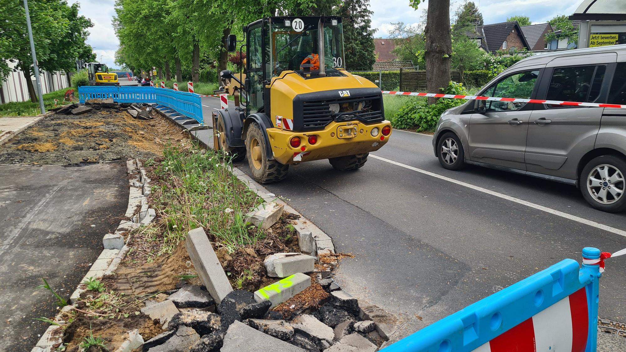 Die Bushaltestelle an der Dansweilerstraße in Glessen wird dargestellt. Ein Baufahrzeug und ein Auto sind vordergründig an einer abgesperrten Baustelle zu sehen.