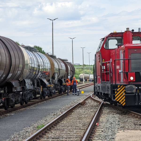 Der Chemiepark Knapsack in Hürth. Zwischen Gleisen und zwei Zügen stehen zwei Gleisarbeiter in orangenen Westen mit Bauhelmen.