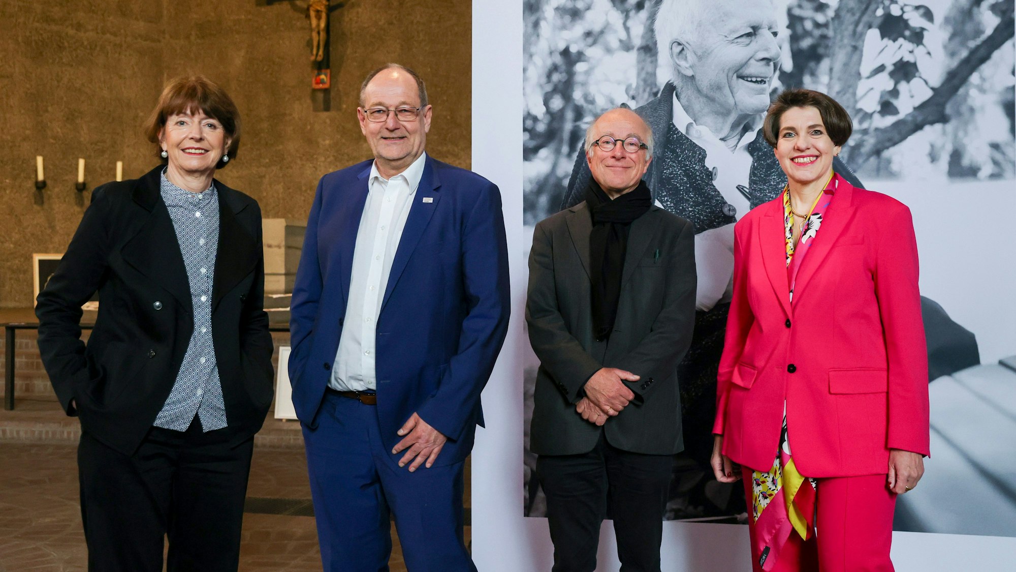 Die vier stehen beim Altar vor einem schwarz-weiß Foto von Gottfried Böhm.