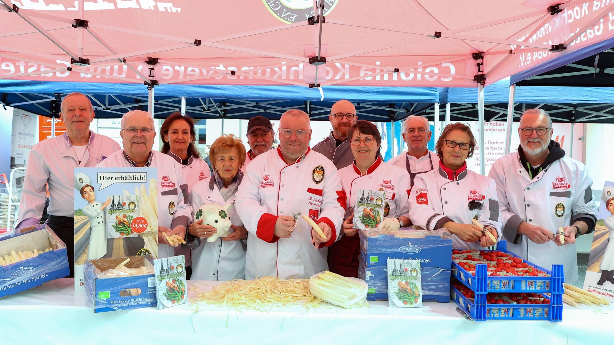 Mehrere Köchinnen und Köche schälen Spargel an einem Stand.