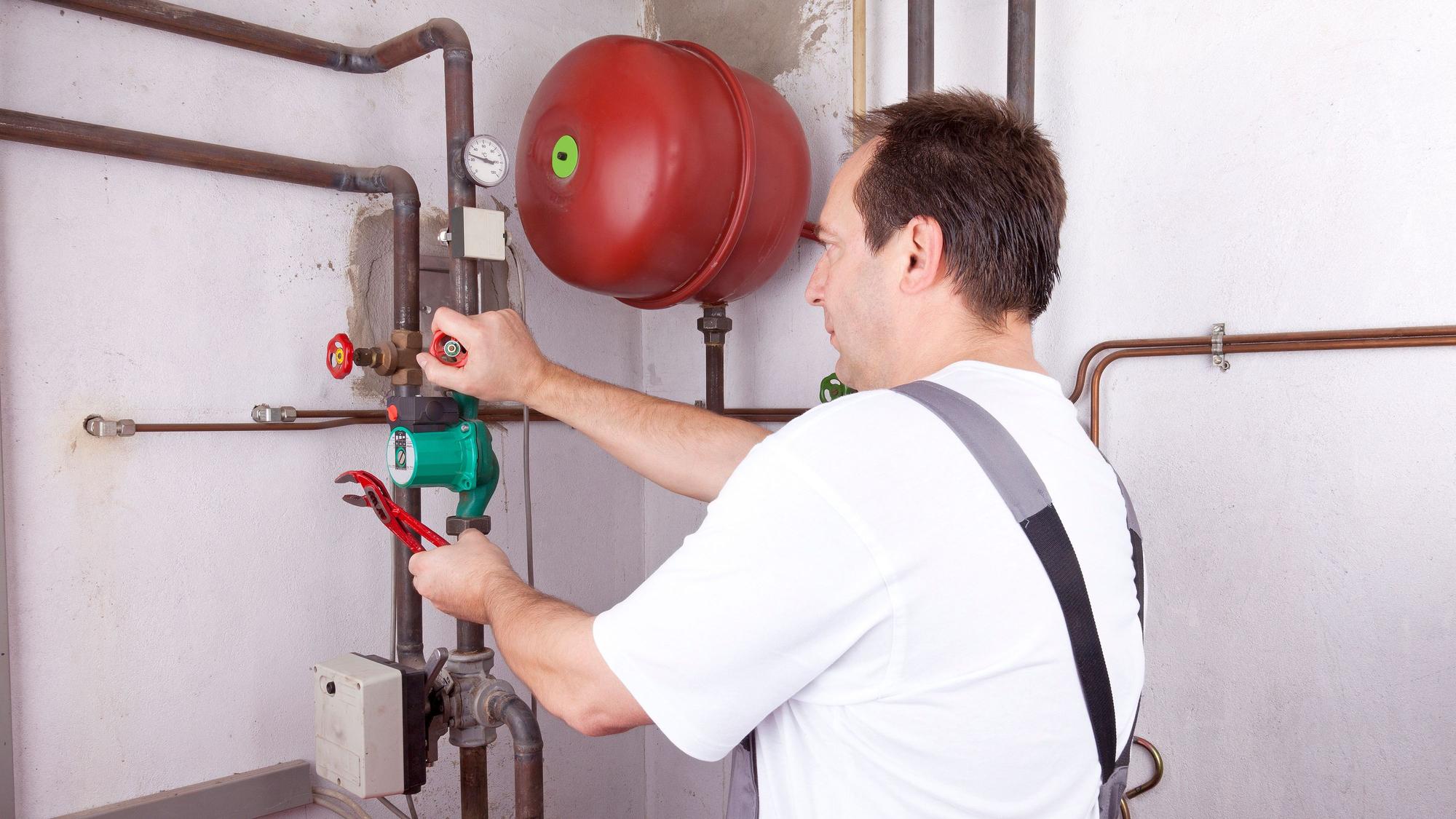 Ein Handwerker arbeitet im Keller an einer Leitung.
