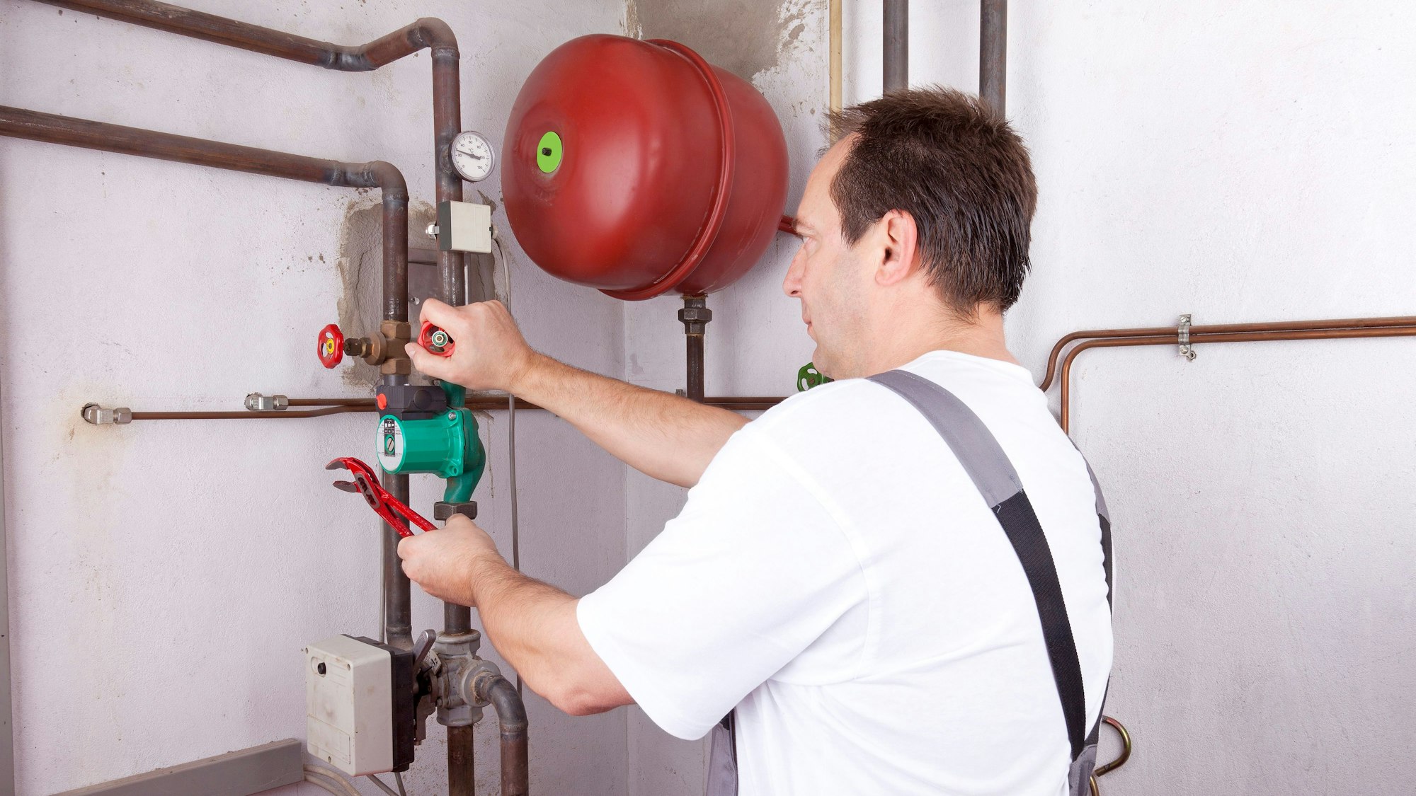 Ein Handwerker arbeitet im Keller an einer Leitung.