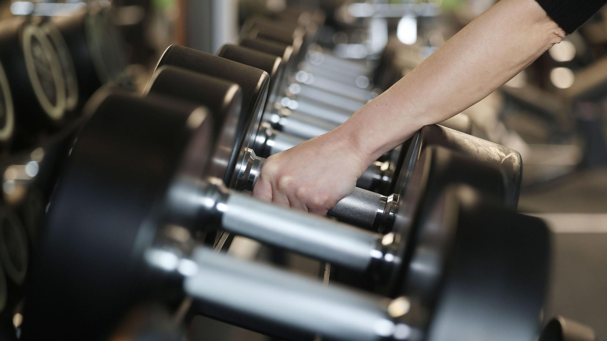 Ein Mensch greift Hanteln in einem Fitnessstudio.