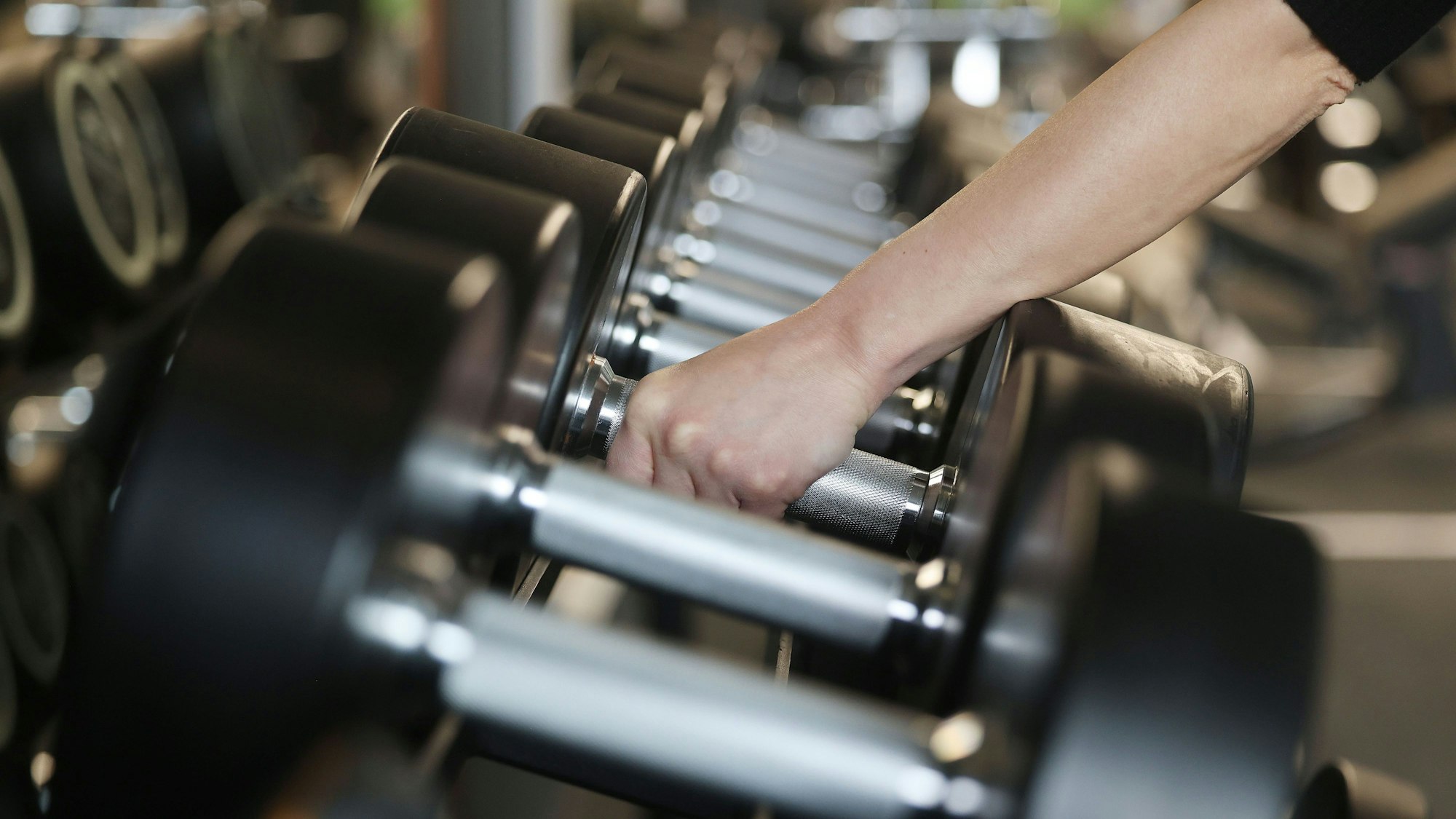 Ein Mensch greift Hanteln in einem Fitnessstudio.