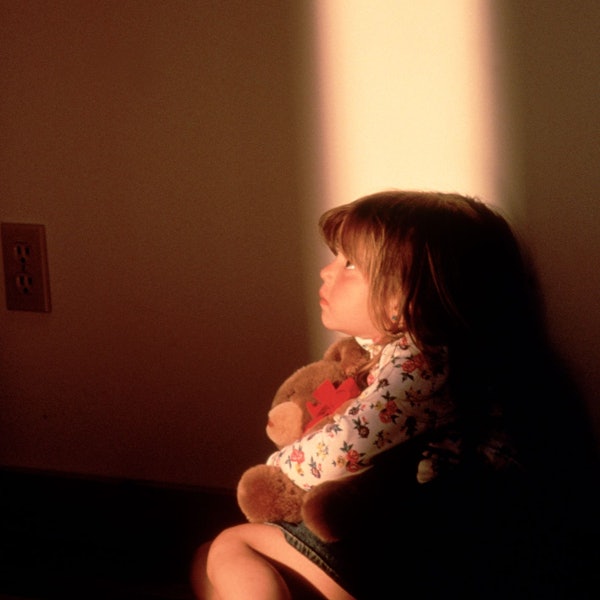 Ein kleines Mädchen hält einen Teddybären in der Hand und schaut beängstigt nach oben