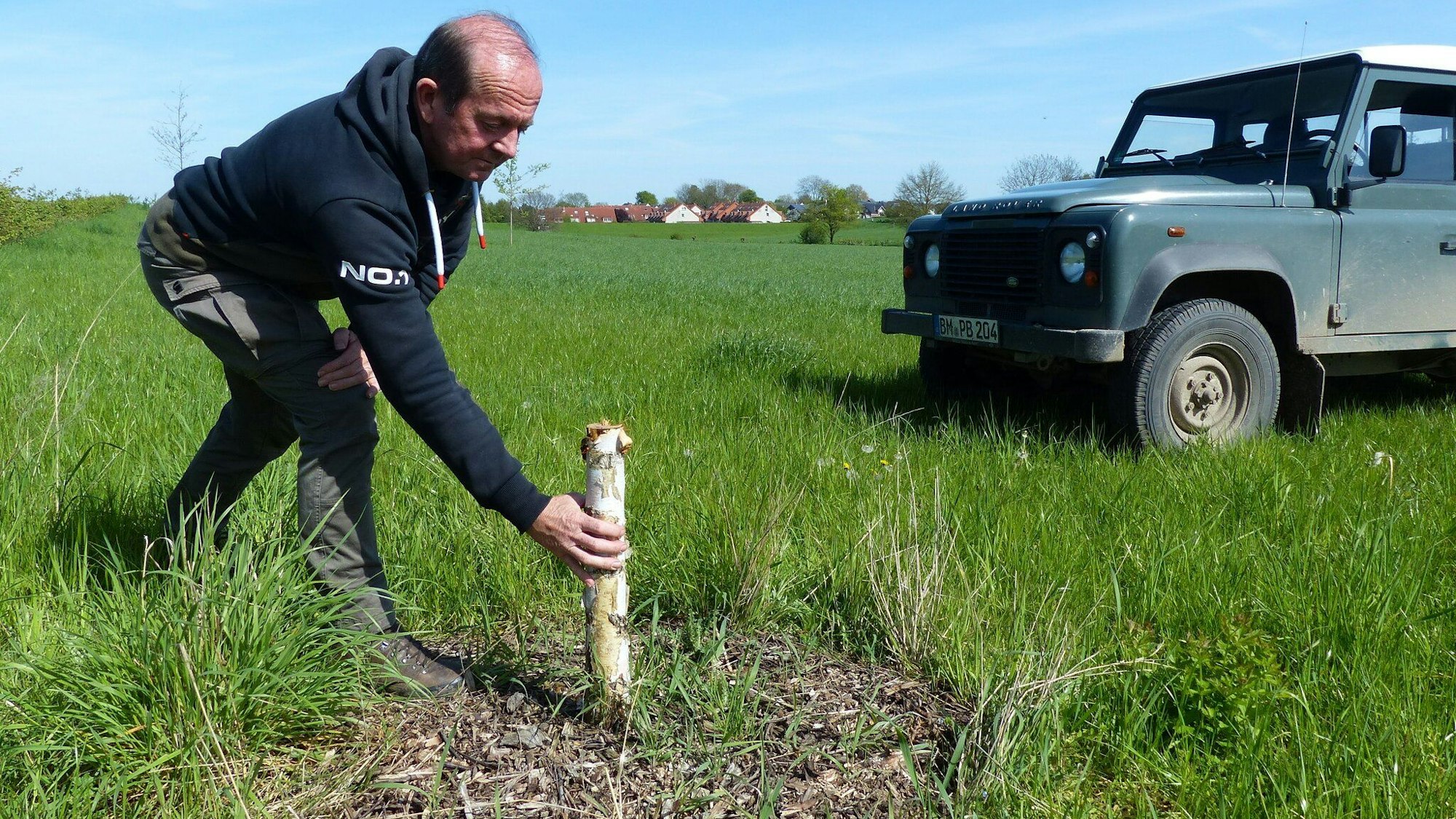 Verbandsmeister Ralf Porschen zeigt den Baumstumpf. Im Hintergrund parkt ein Auto.