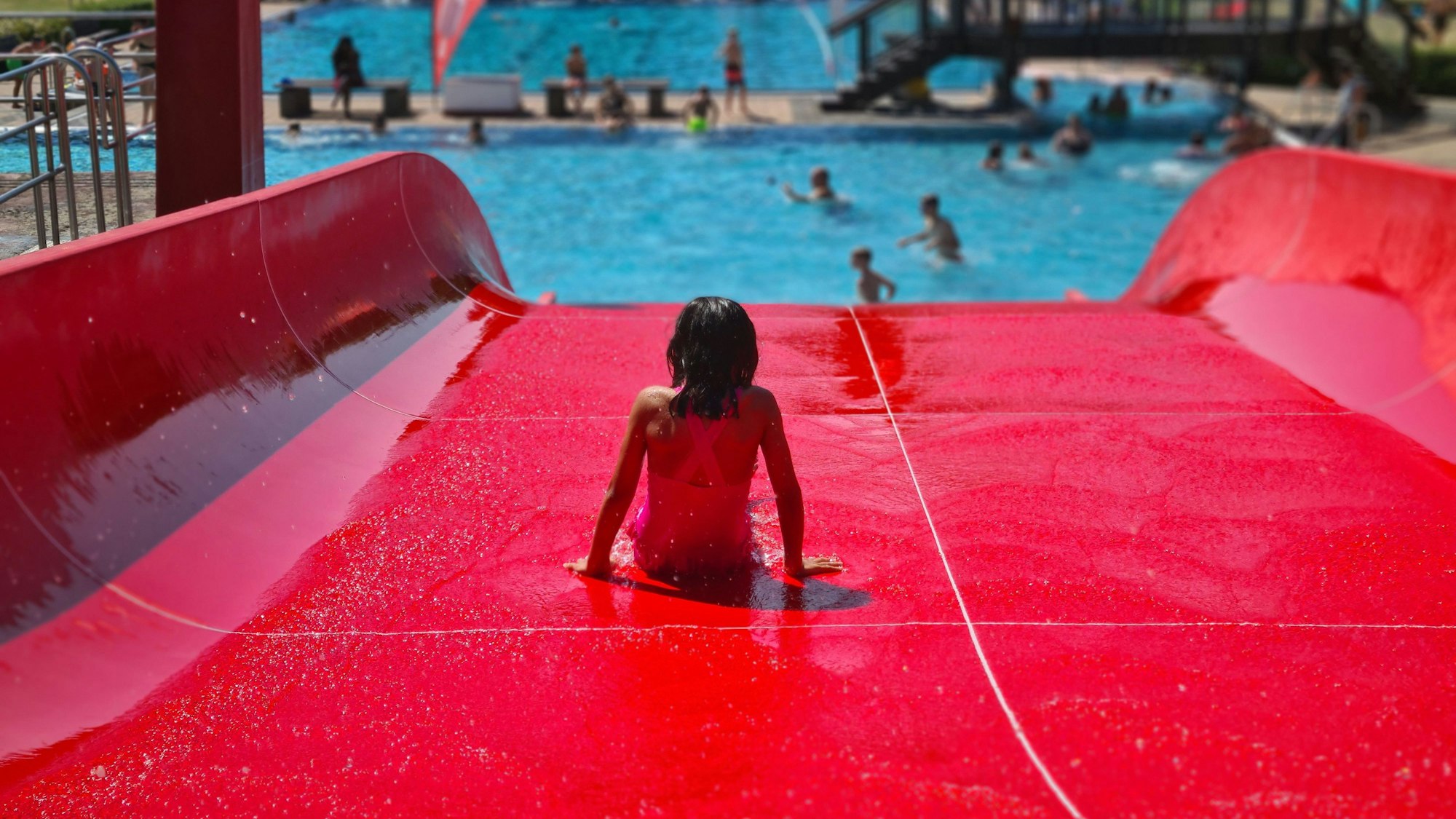 Das Foto zeigt ein kleines Mädchen, das auf einer roten Rutsche im Bedburger Freibad ins Wasser rutscht.
