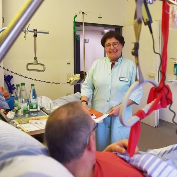 Marianne Kesseler steht in einem grünen Kittel am Bett eines Patienten in einem Zwei-Bett-Zimmer der Unfallstation im Kreiskrankenhaus Mechernich.