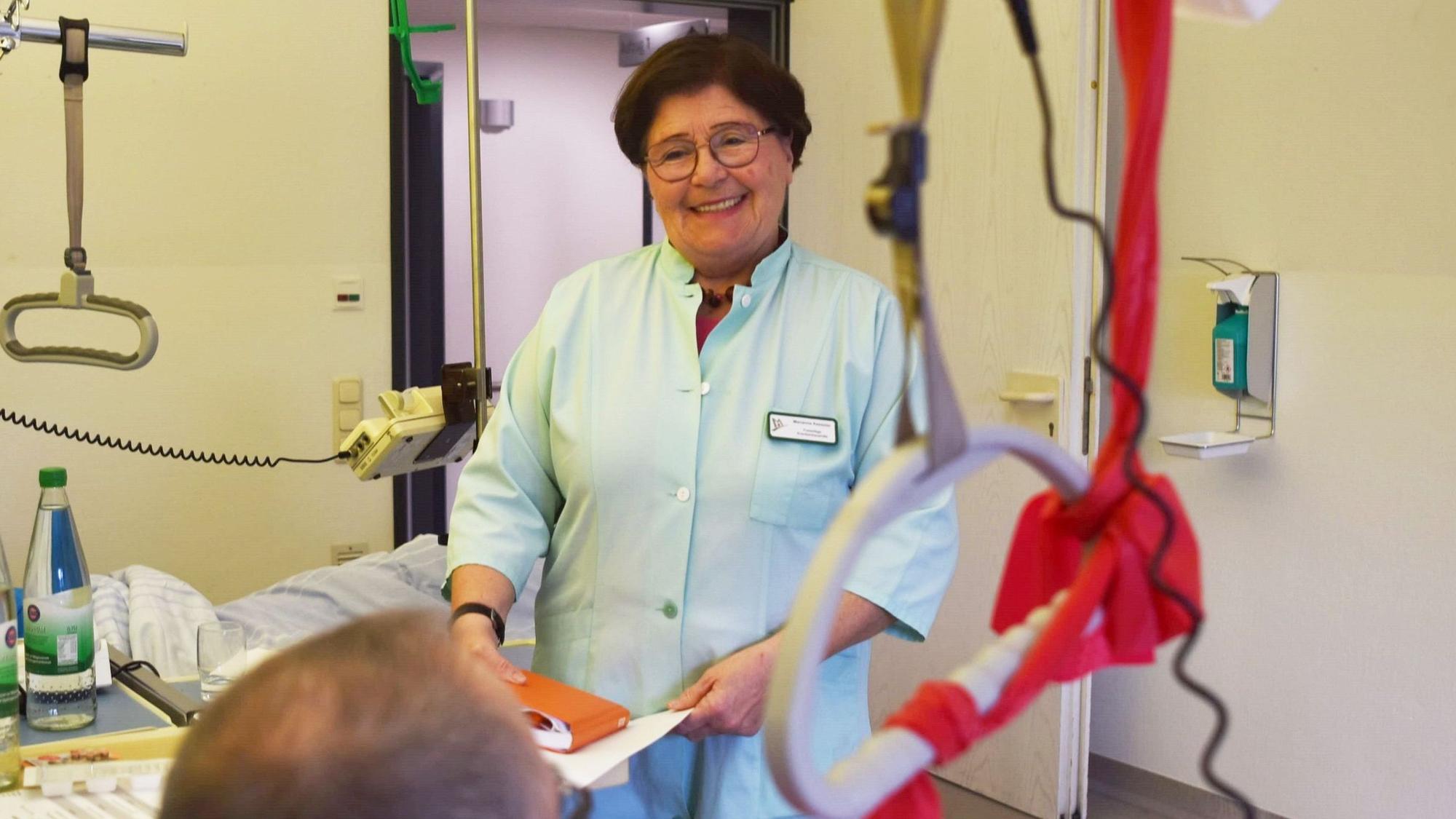 Marianne Kesseler steht in einem grünen Kittel am Bett eines Patienten in einem Zwei-Bett-Zimmer der Unfallstation im Kreiskrankenhaus Mechernich.