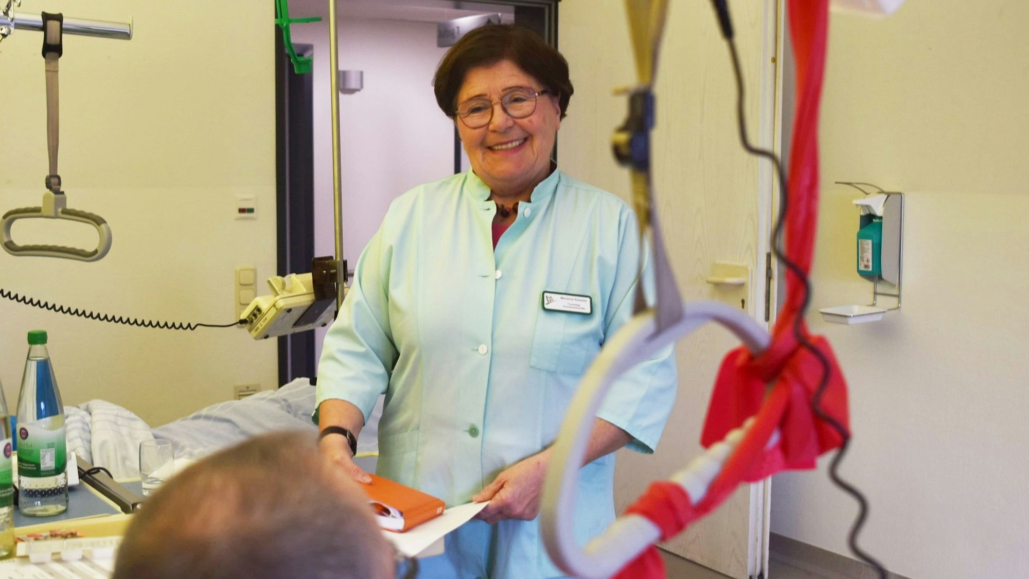 Marianne Kesseler steht in einem grünen Kittel am Bett eines Patienten in einem Zwei-Bett-Zimmer der Unfallstation im Kreiskrankenhaus Mechernich.