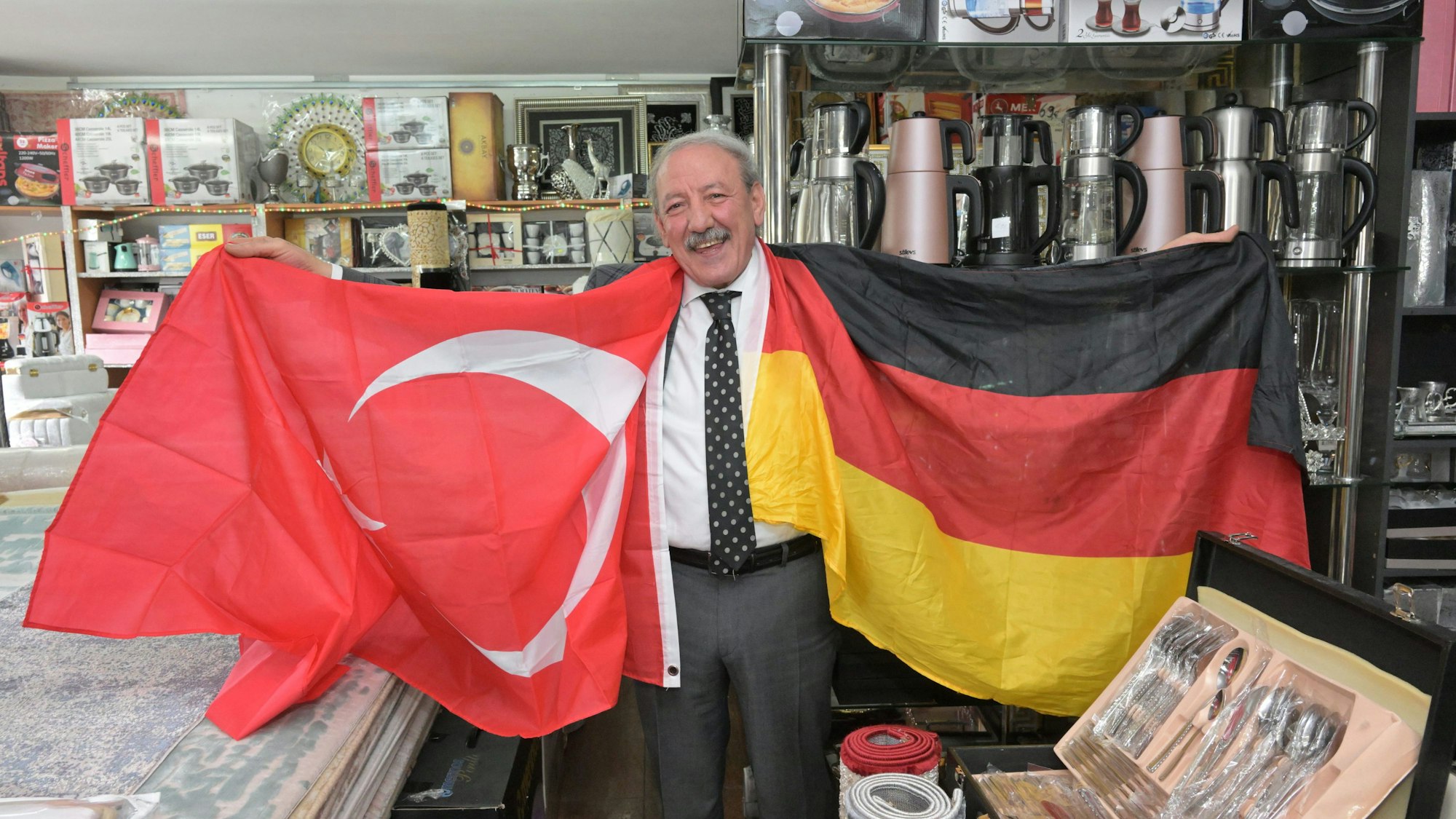 Hasan Ata, Inhaber des Teppichgeschäfts Gonau. Er hält zwei Fahnen in den Händen, eine türkische und eine deutsche.