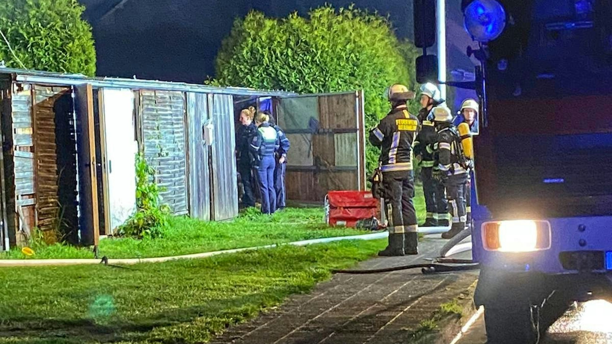 Das Foto zeigt Feuerwehrleute und Polizisten, die die Laube begutachten, nachdem das Feuer gelöscht worden war.