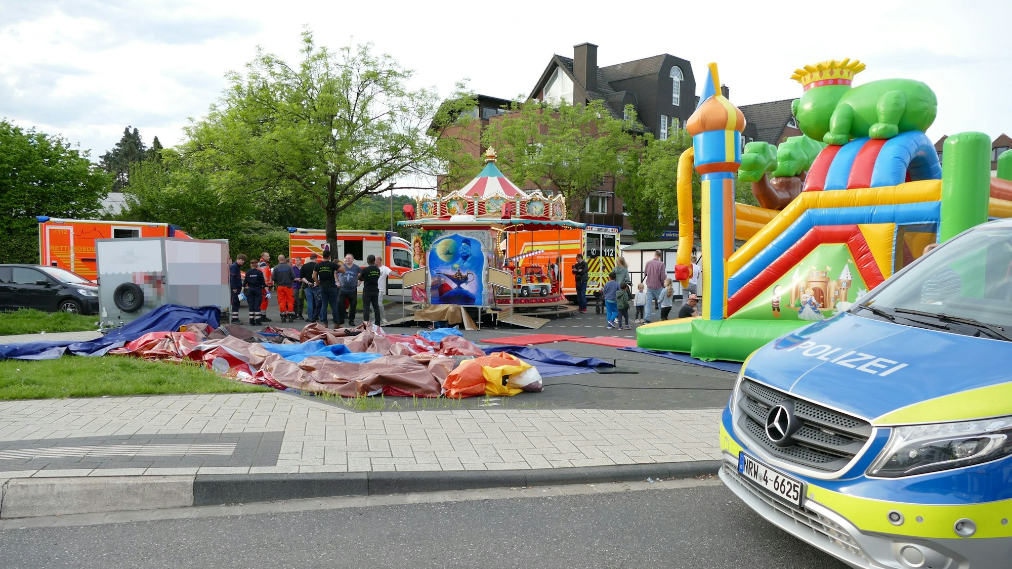 Die Hüpfburg liegt auf dem Boden. Im Hintergrund sind ein Karussell und die Rettungskräfte zu sehen. Im Vordergrund ein Polizeiwagen.