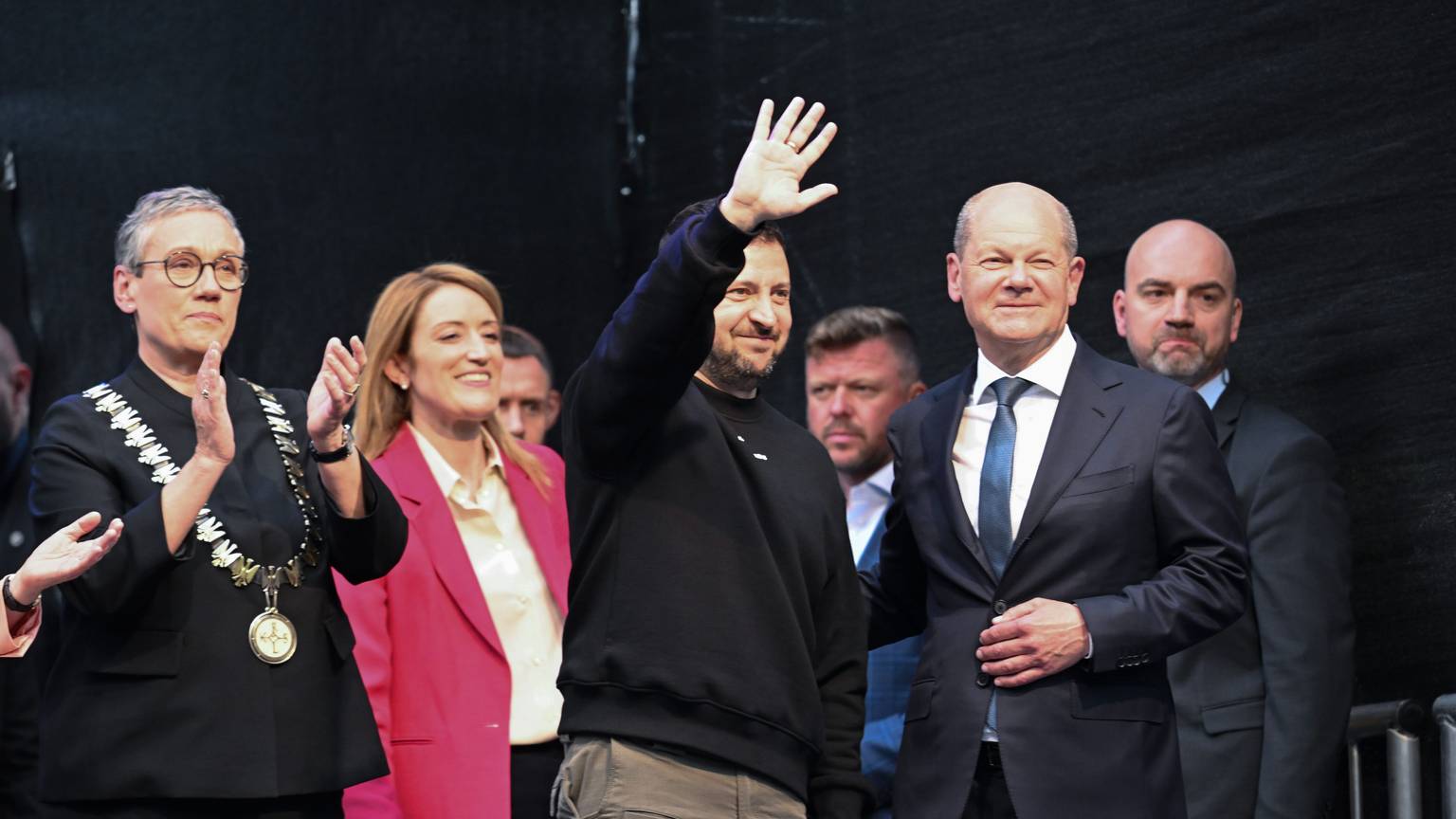 Der ukrainische Präsident und Preisträger Wolodymyr Selenskyj (M) bekommt Applaus und winkt den Menschen vor dem Rathaus nach der Verleihung des Karlspreises für Verdienste um die Einheit Europas. Links Oberbürgermeisterin Sibylle Keupen (parteilos) und Roberta Metsola, EU-Parlamentspräsidentin, 2.v.r Bundeskanzler Olaf Scholz (SPD).