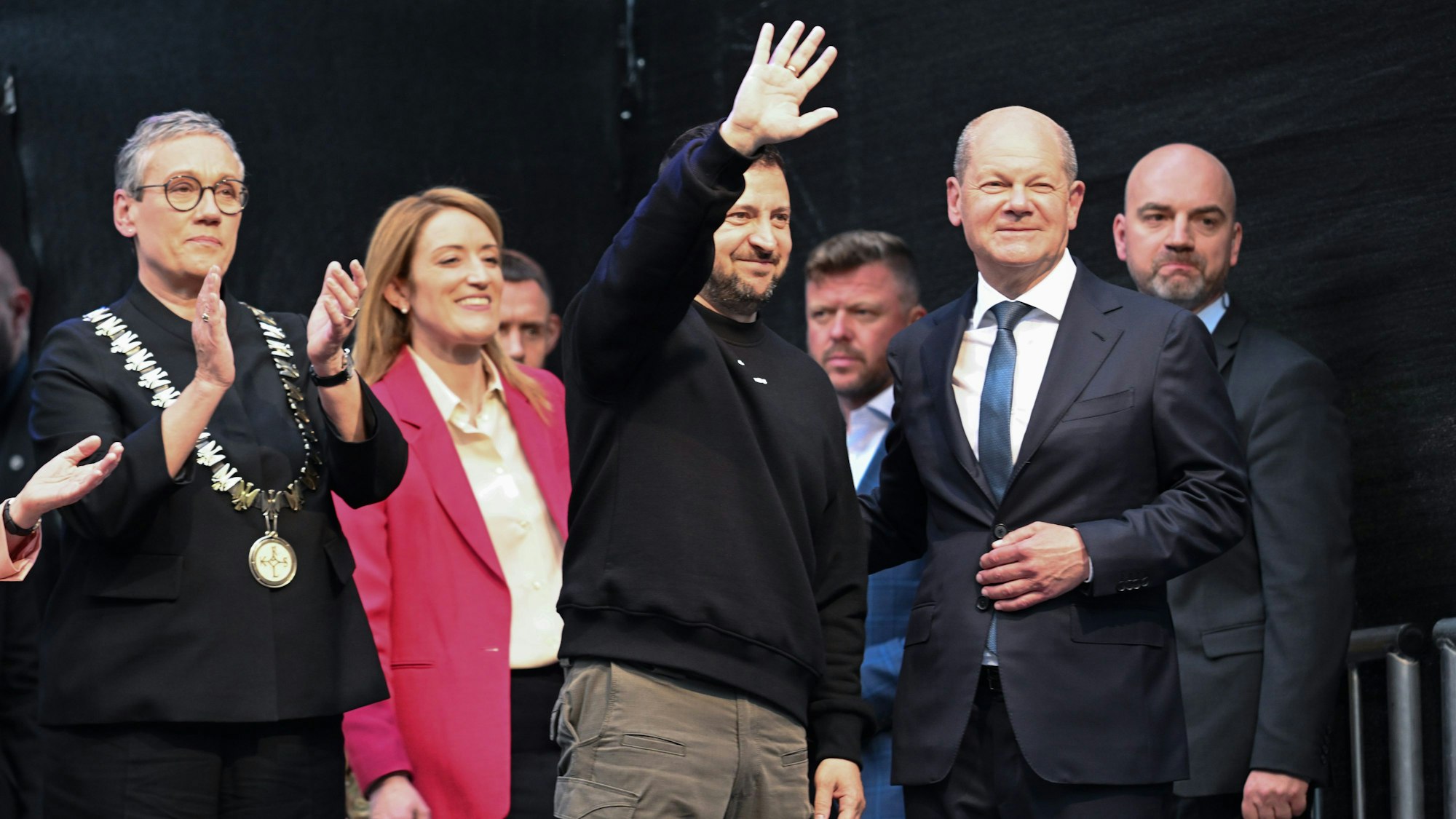 Der ukrainische Präsident und Preisträger Wolodymyr Selenskyj (M) bekommt Applaus und winkt den Menschen vor dem Rathaus nach der Verleihung des Karlspreises für Verdienste um die Einheit Europas. Links Oberbürgermeisterin Sibylle Keupen (parteilos) und Roberta Metsola, EU-Parlamentspräsidentin, 2.v.r Bundeskanzler Olaf Scholz (SPD).