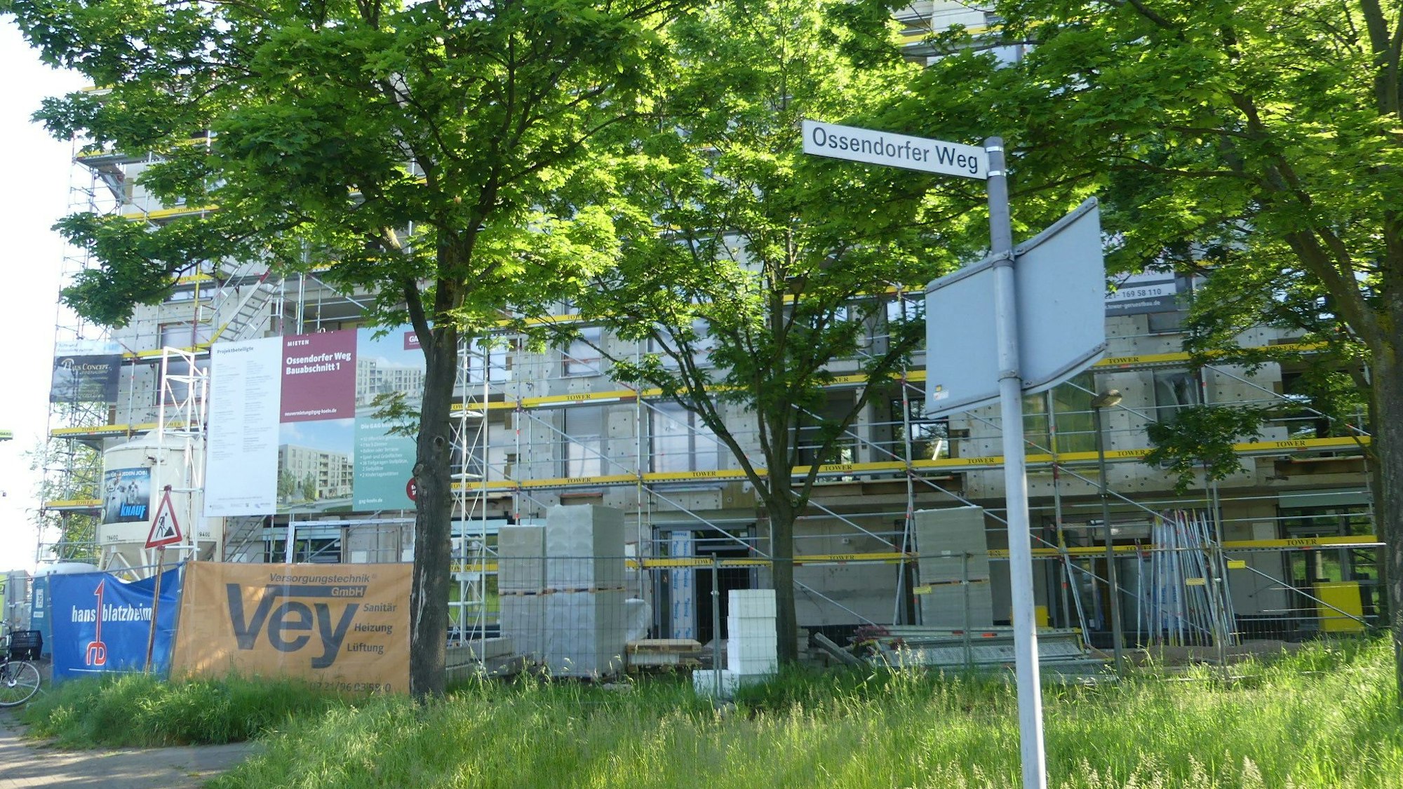 Hinter den Bäumen sind die Neubauten zu sehen, um die ein Gerüst aufgebaut sind.