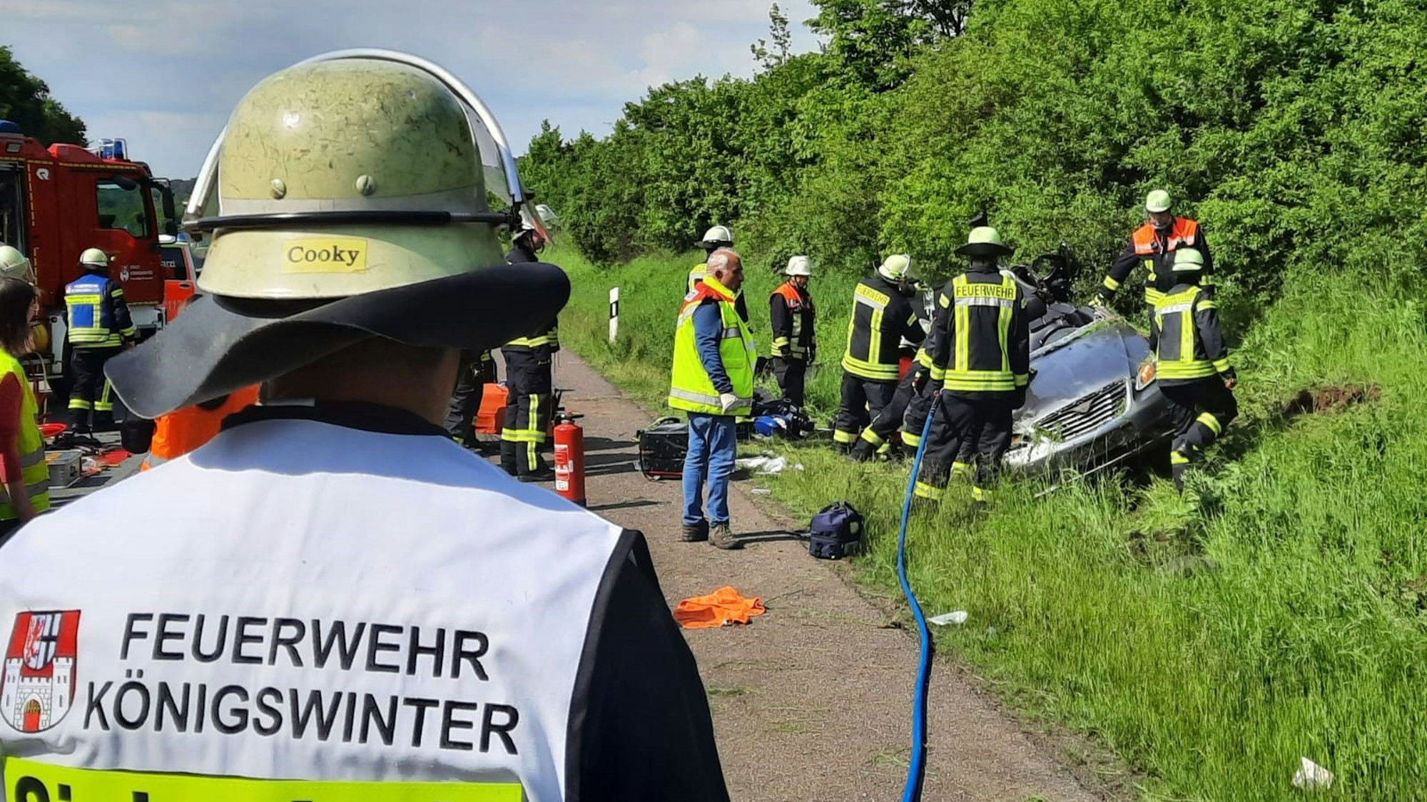 Ein Feuerwehrmann steht mit dem Rücken zur Kamera und schaut auf das in der Böschung liegende Auto, das von Einsatzkräften umringt ist.