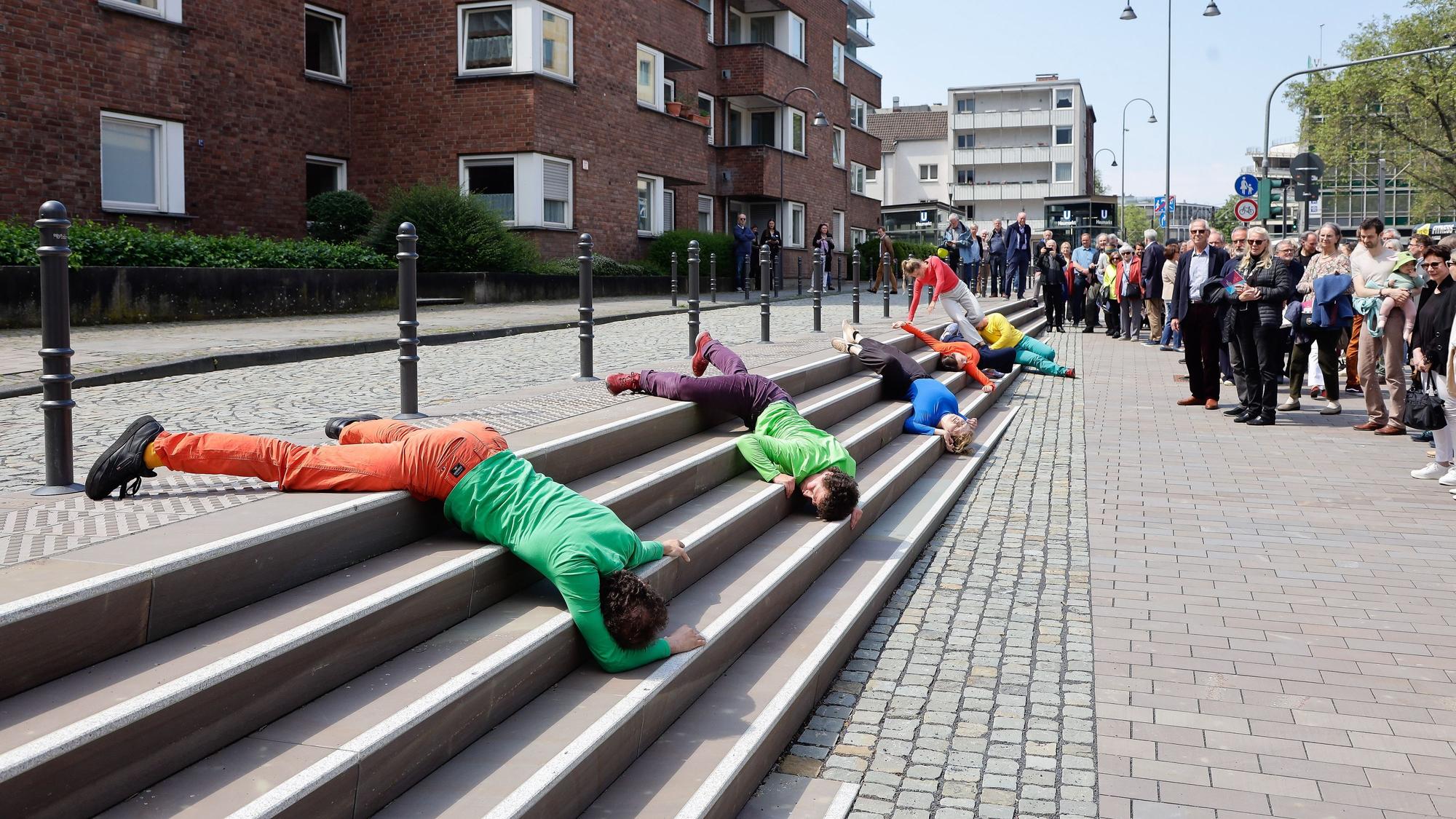 Tänzer liegen in bunter Kleidung auf der Treppe.