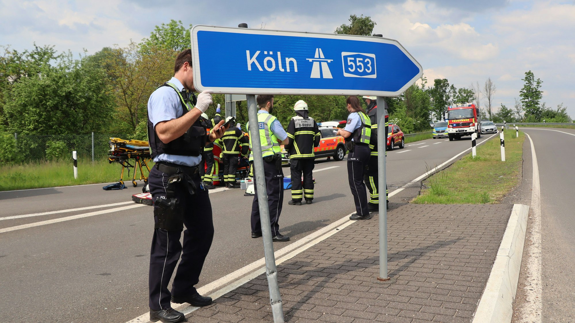 Das Foto zeigt ein blaues Hinweisschild, das auf die A 553 weist. Ein Polizist versucht, es zu richten, nachdem der 50-Jährige mit seinem Quad dagegen gefahren war.