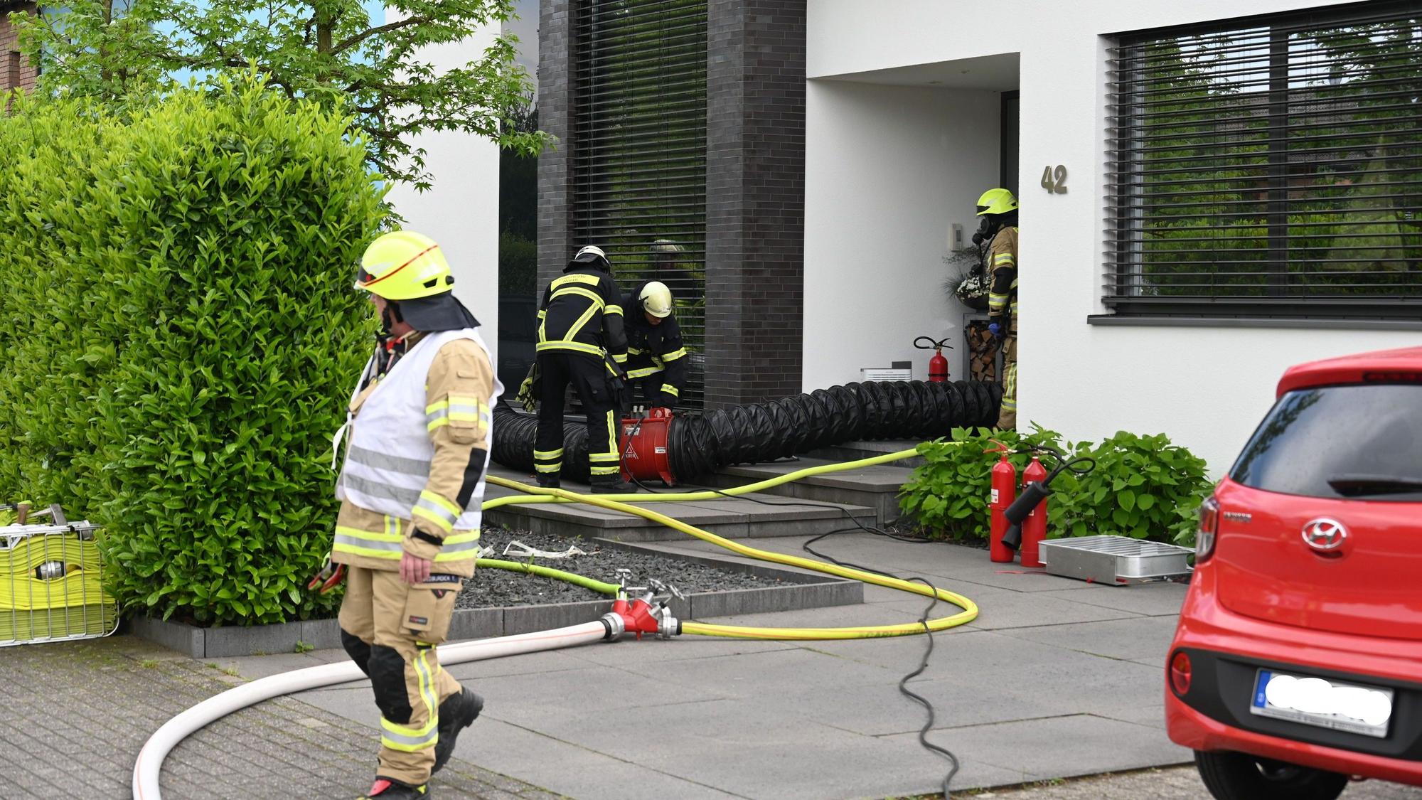 Feuerwehrleute laufen vor einem Hauseingang. In das Haus hinein führt ein Schlauch.