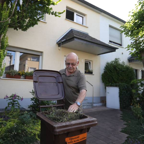 Ein Mann greift vor einem Haus in eine Mülltonne.