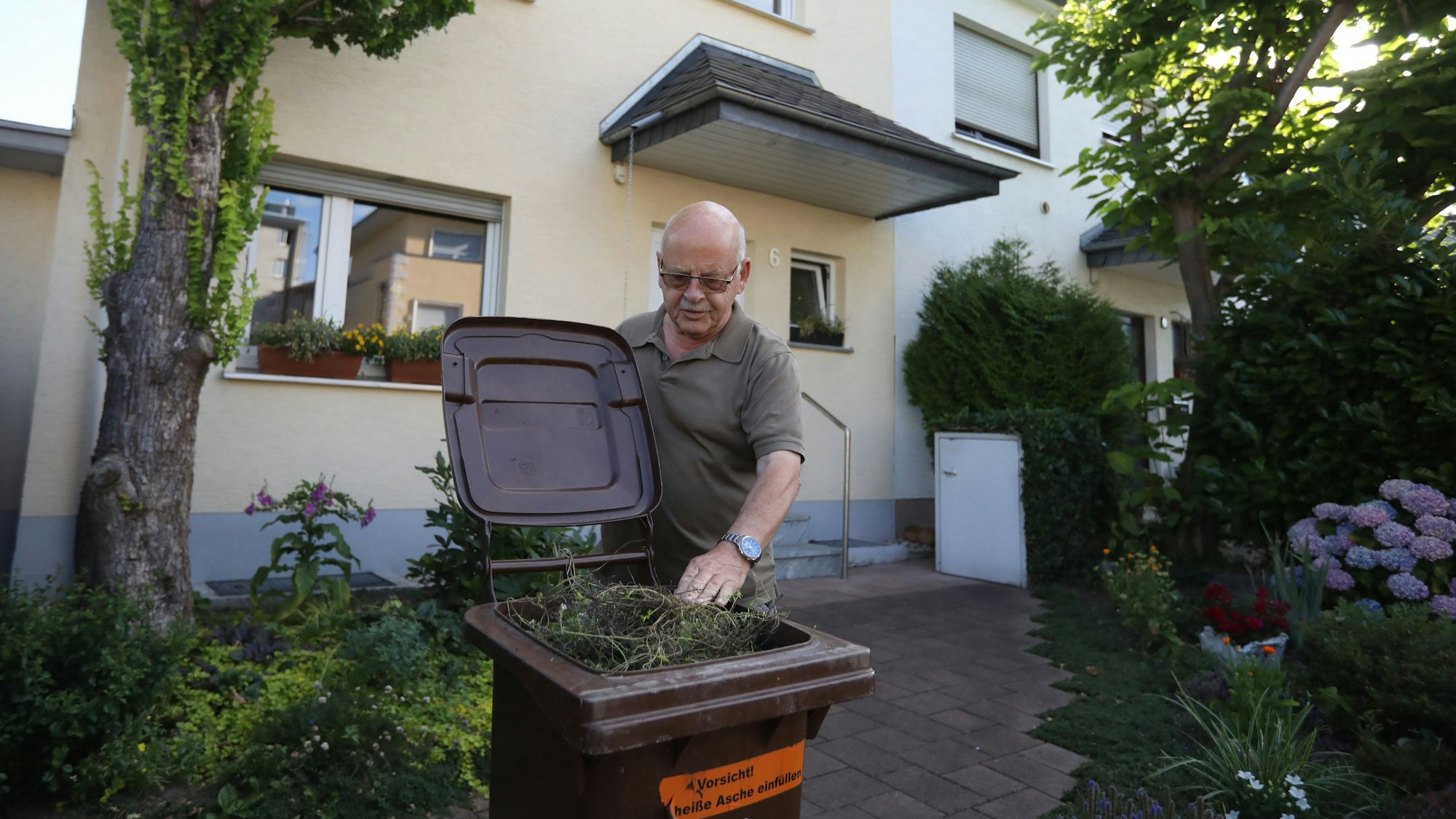 Ein Mann greift vor einem Haus in eine Mülltonne.