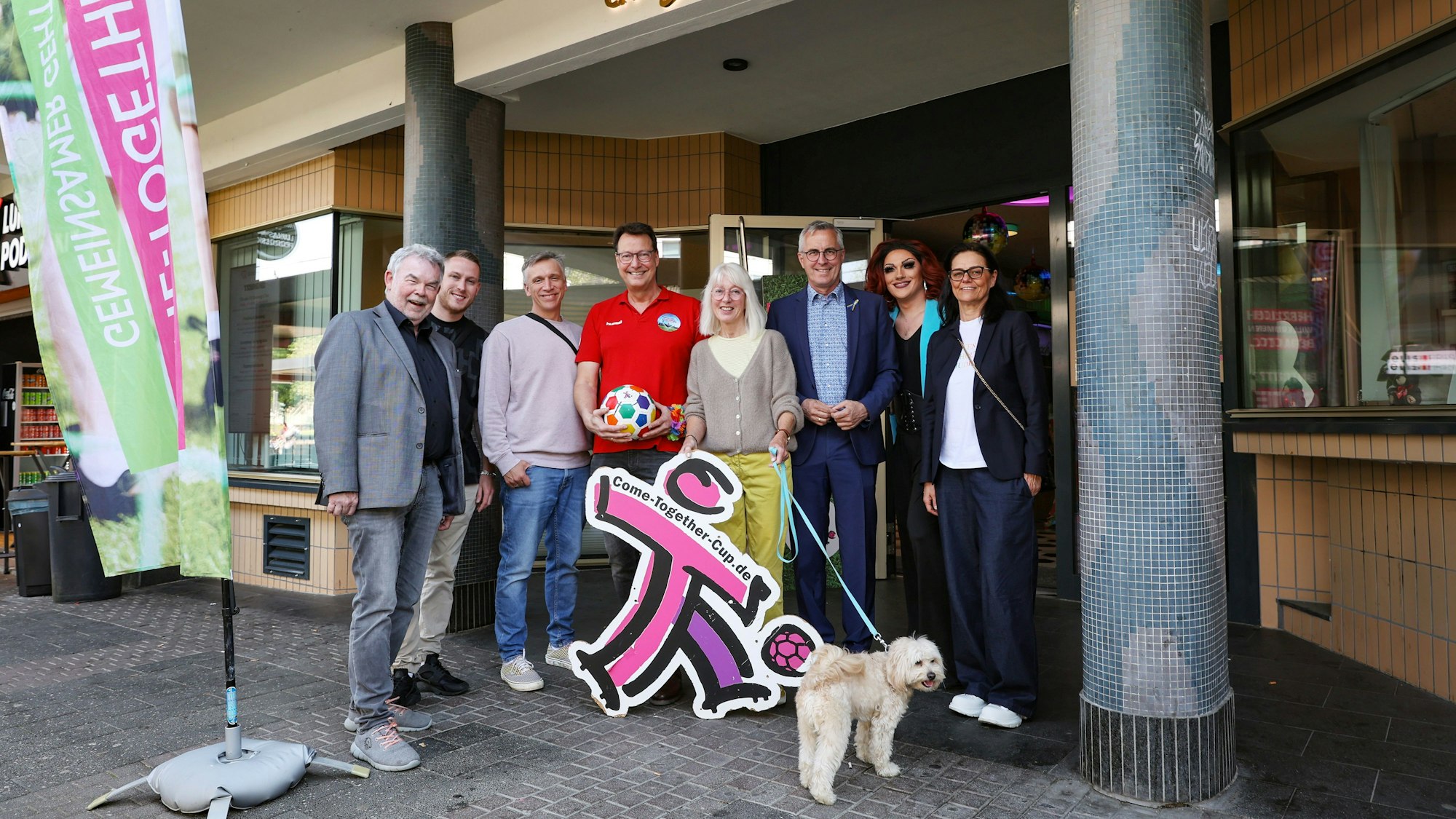 Die Botschafter des CTC stehen vor dem Cafe Bach in Köln, neben ihnen eine Fahne des CTC.