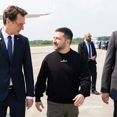 Der ukrainische Präsident Wolodymyr Selenskyj wird von NRW-Ministerpräsident Hendrik Wüst auf dem Nato-Flugplatz in Geilenkirchen empfangen. Anschließend geht es mit einer Polizeieskorte nach Aachen zur Karlspreis-Verleihung. Im Hintergrund stehen ukrainische Militärangehörige und Sicherheitspersonal.