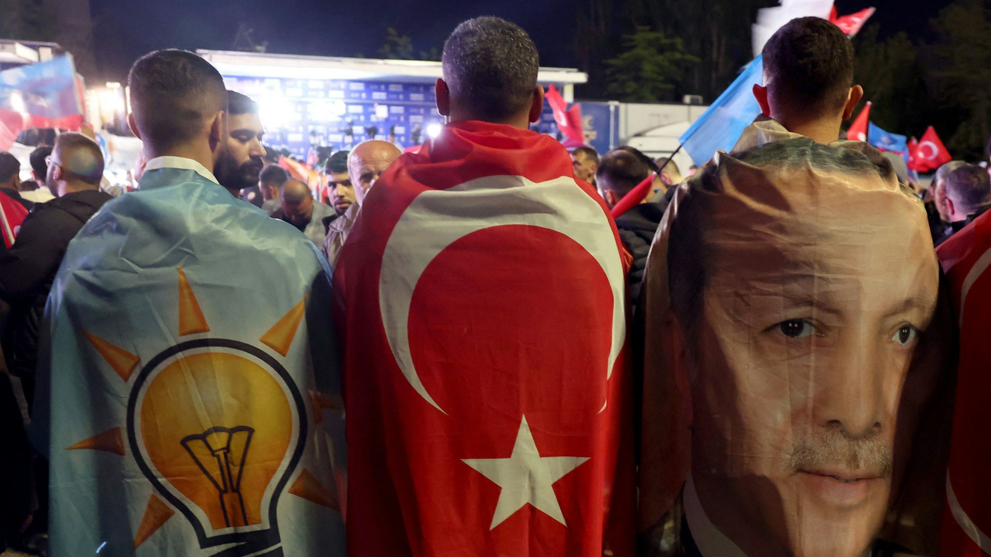Unterstützer von Tayyip Erdogan vor der Parteiszentrale in Ankara. Die Männer sind in dir türkische Flagge, in ein Banner mit Erdogans Konterfei und in eine Flagge mit dem Logo der AK bekleidet.