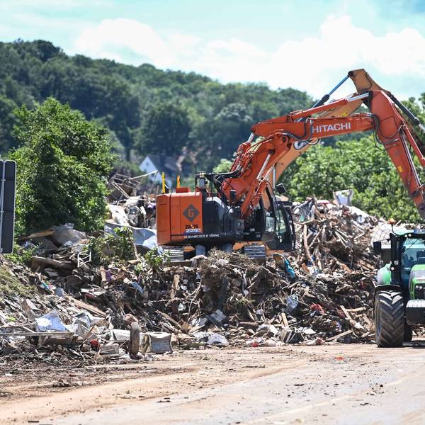 Ein Bagger steht auf einem Müllberg und lädt Sperrmüll in einen Lkw und einen Traktor.
