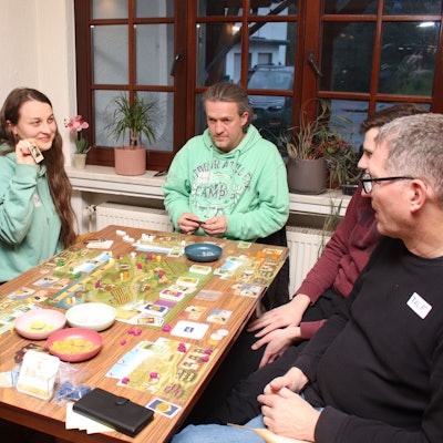 Mehrere Personen sitzen an einem Tisch mit einem Brettspiel.