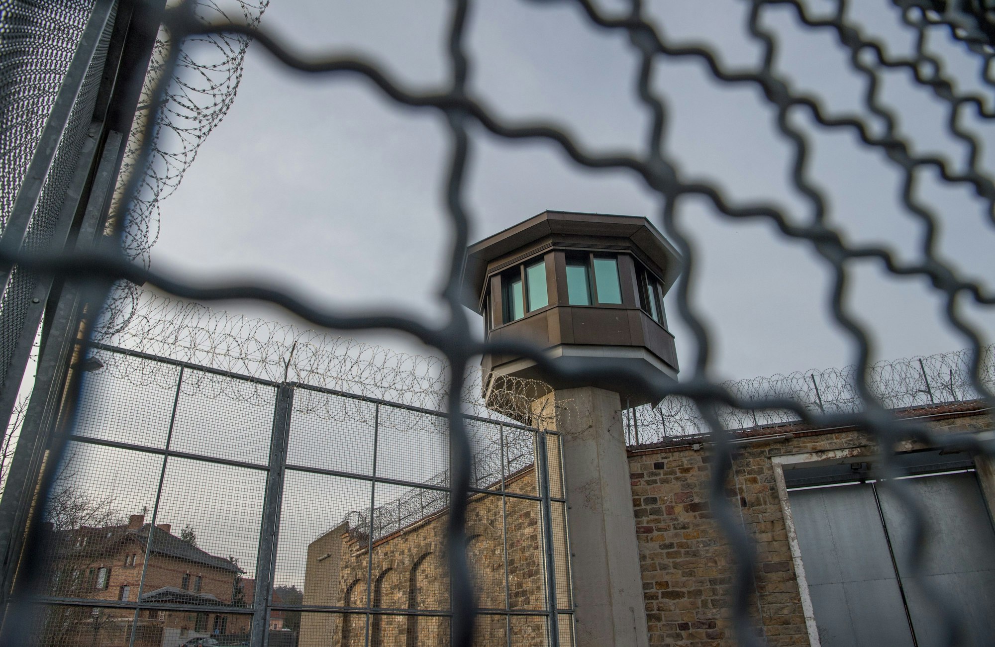 Mauern und Stacheldraht an einer JVA, im Hintergrund ist ein Wachturm zu sehen.