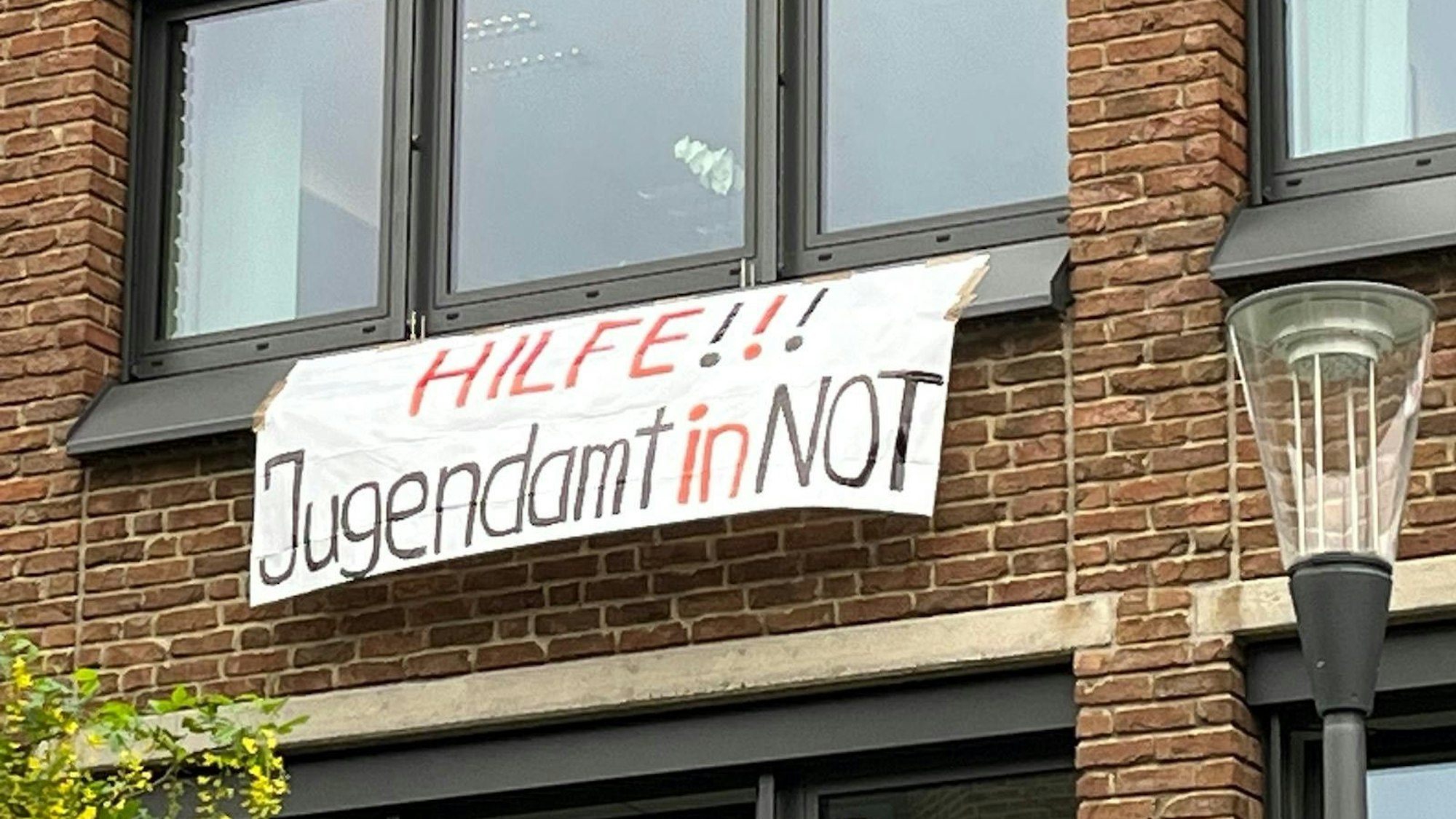 Ein weißes Transparent mit der Aufschrift "Hilfe!!! Jugendamt in Not" hängt am Bezirksjugendamt in Chorweiler.