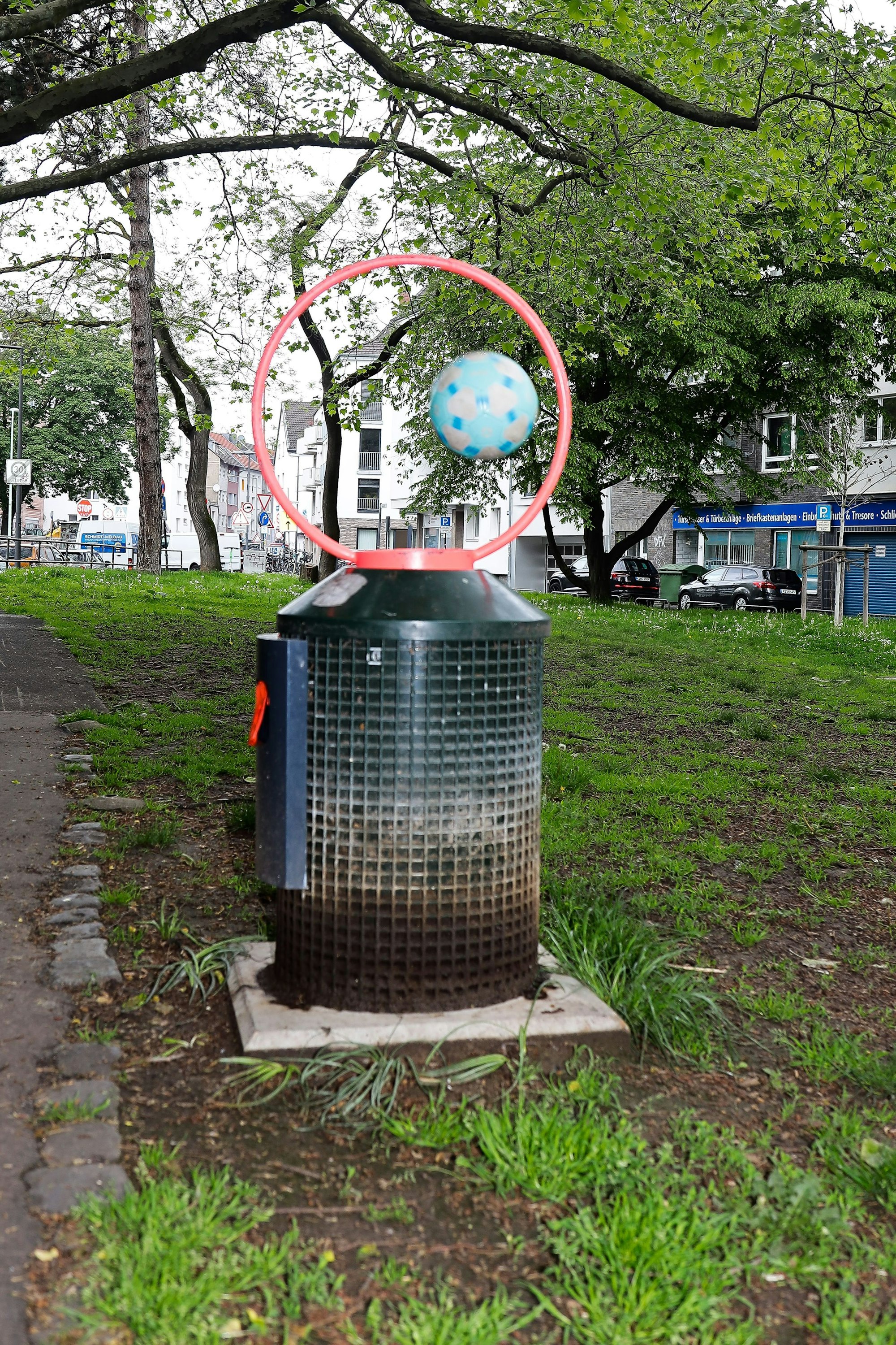 Ein Fußball fliegt durch einen runden Stahlaufsatz, der auf einem Mülleimer befesigt ist.