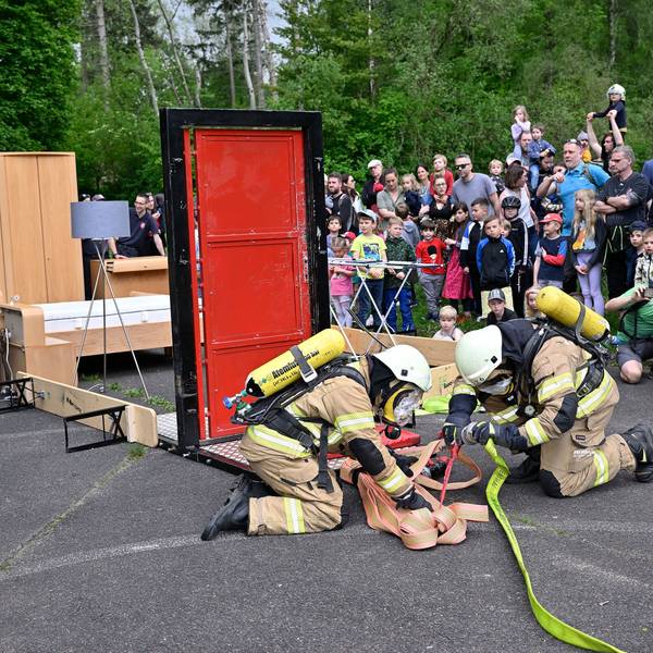 Feuerwehrleute montieren einen Feuerwehrschlauch. Im Hintergrund beobachten Zuschauer die Szenerie.