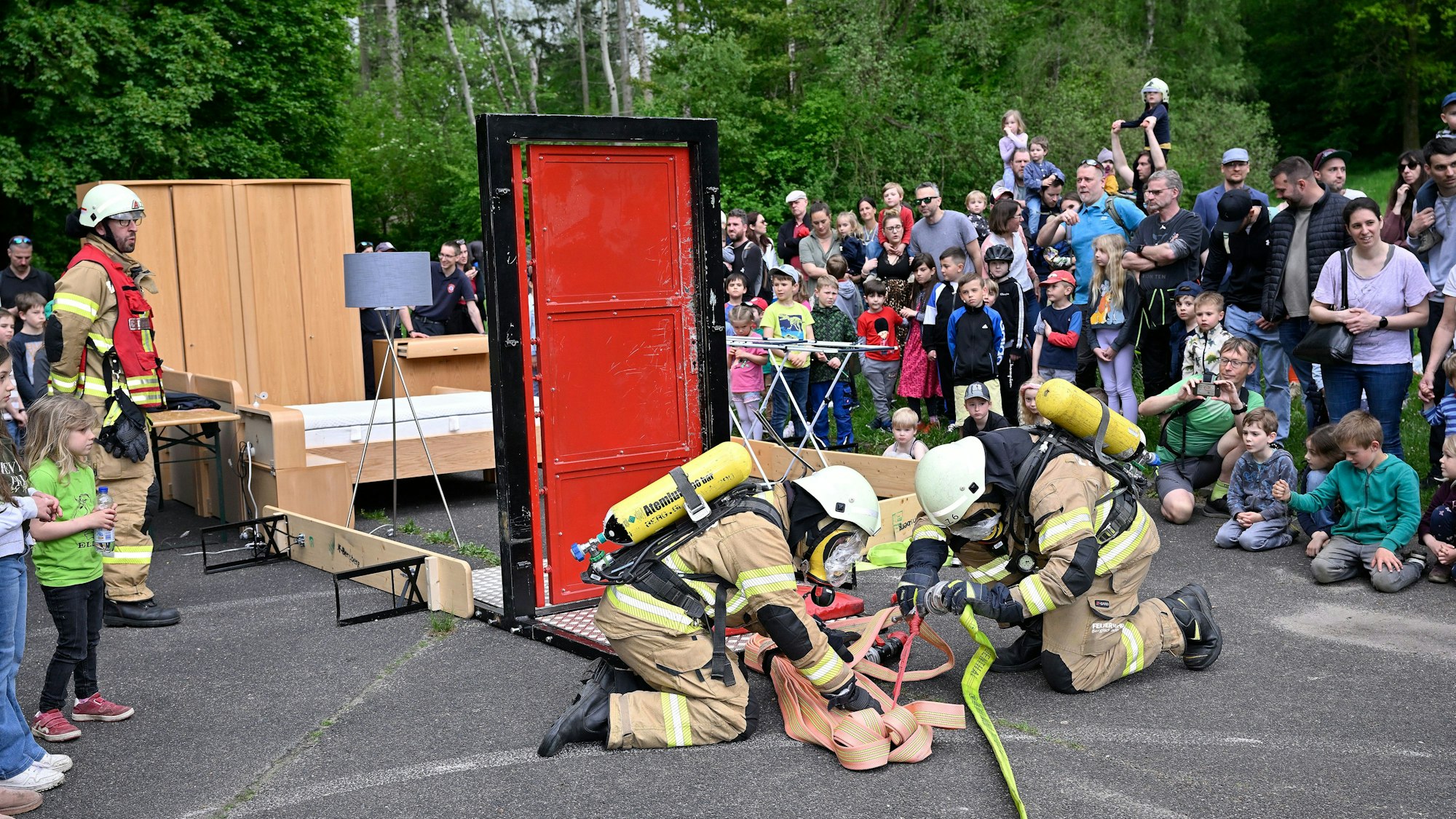 Feuerwehrleute montieren einen Feuerwehrschlauch. Im Hintergrund beobachten Zuschauer die Szenerie.