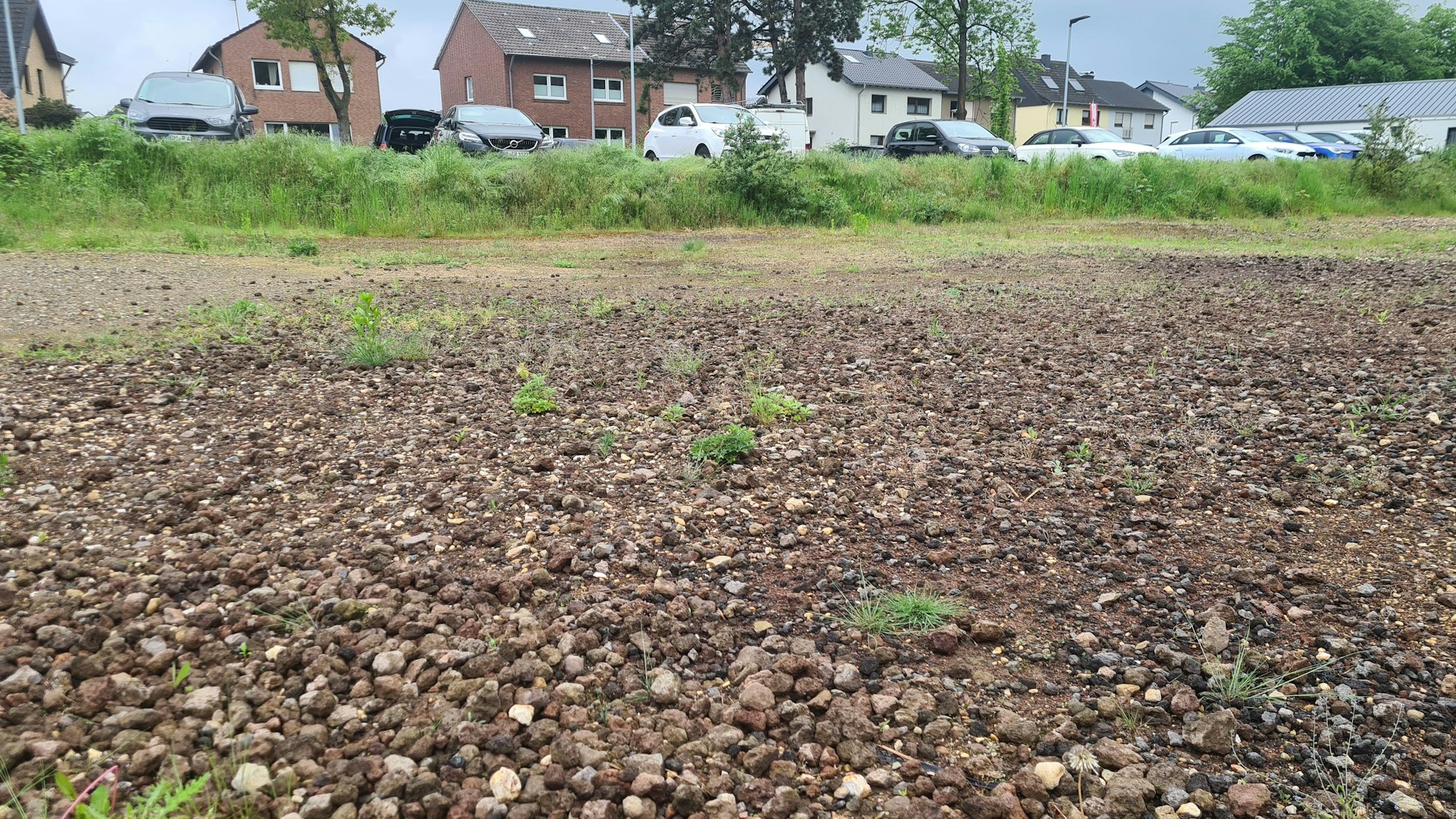 Die Fläche des alten Sportplatzes in Lipp. Es ist eine Schotterfläche zu sehen, im Hintergrund parken Autos und stehen Häuser.