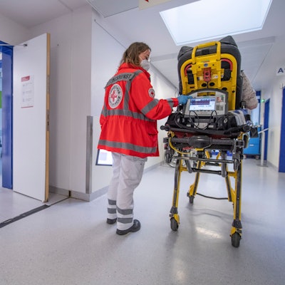 Ein Notfallsanitäterin schiebt eine Seniorin nach einem Schlaganfall auf einer Trage in die Notaufnahme eines Krankenhauses.