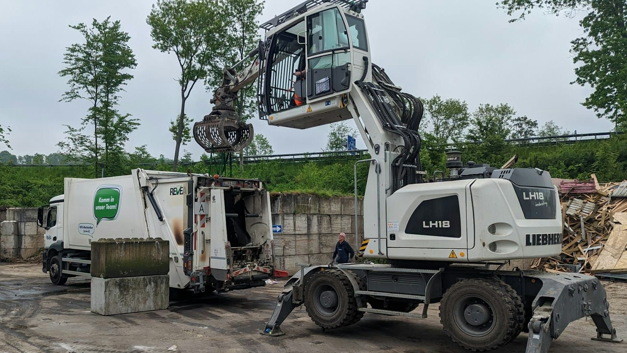 Ein Bagger steht neben einem Müllsammelfahrzeug, in dem es gebrannt hat, wie Rußspuren zeigen.