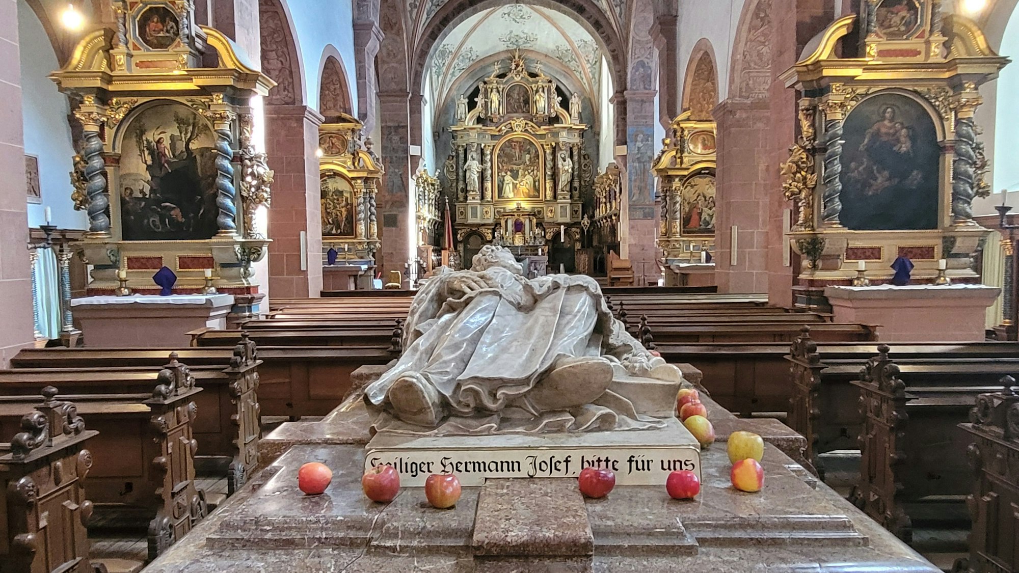 Blick auf den Marmorsarkophag der heiligen Hermann Josef, auf dem einige Äpfel liegen.