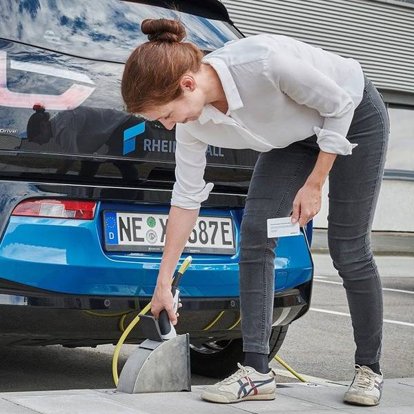 Eine Frau lädt ihr blaues E-Auto an einer Ladestation im Bordstein.