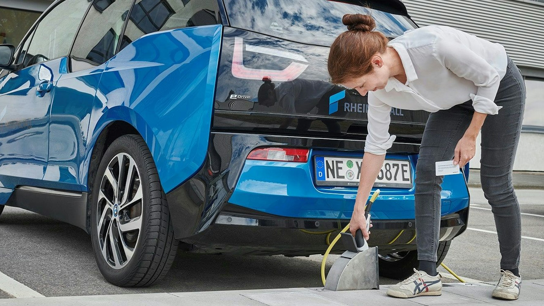 Eine Frau lädt ihr blaues E-Auto an einer Ladestation im Bordstein.