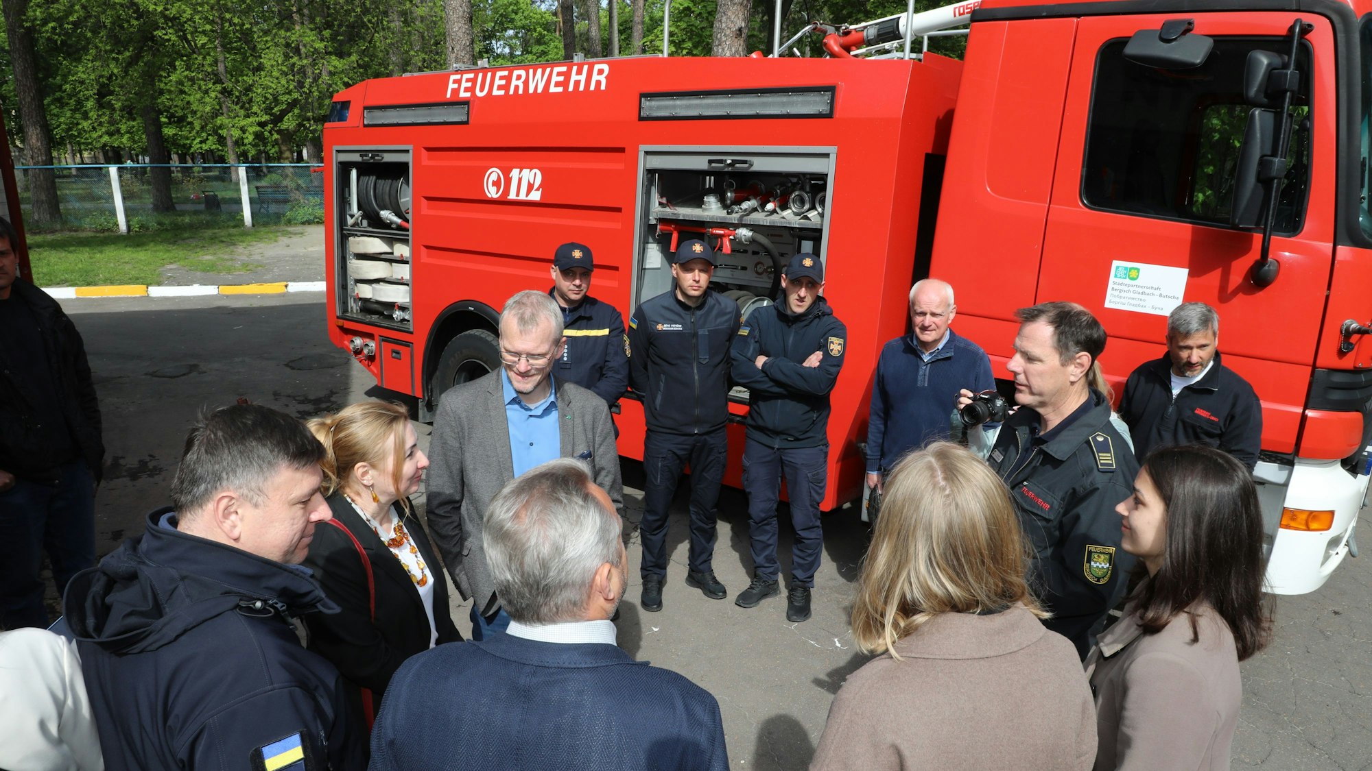 Feuerwehrleute und Zivilisten stehen in einem Kreis vor einem Tanklöschfahrzeug.