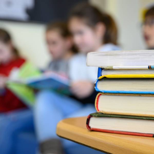 Kinder sitzen hinter einem Stapel Bücher und lesen.
