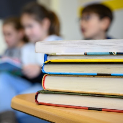 Kinder sitzen hinter einem Stapel Bücher und lesen.