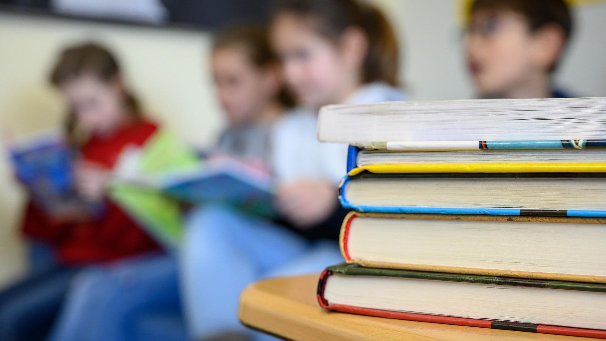 Kinder sitzen hinter einem Stapel Bücher und lesen.