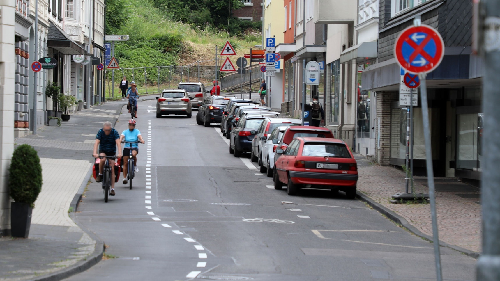 Links auf dem Foto sind Radfahrer auf dem Radstreifen unterwegs. Auf dem Parkstreifen rechts im Bild parken Autos. Auf der Fahrbahn in der Mitte fahren Autos.